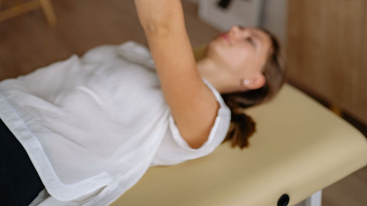 Une personne allongée sur une table de soin, un bras tendu vers le haut soutenu par la main du praticien